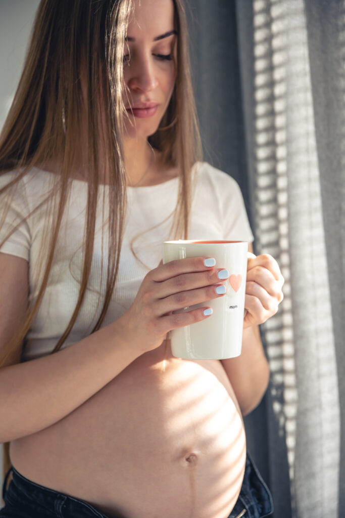 An attractive pregnant woman with a cup of tea at the window in the morning.