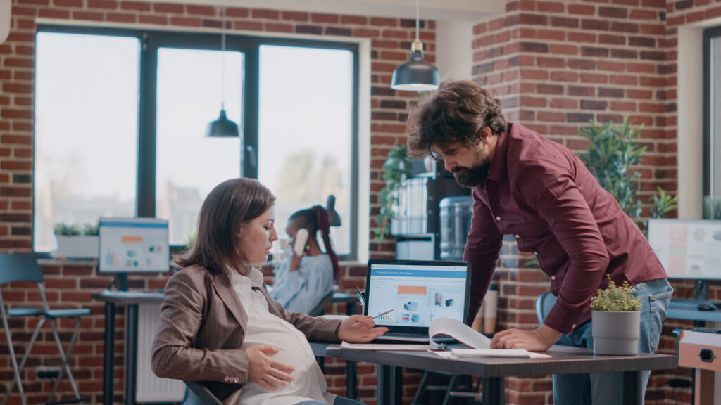 Business woman expecting child and having discussion with man while working