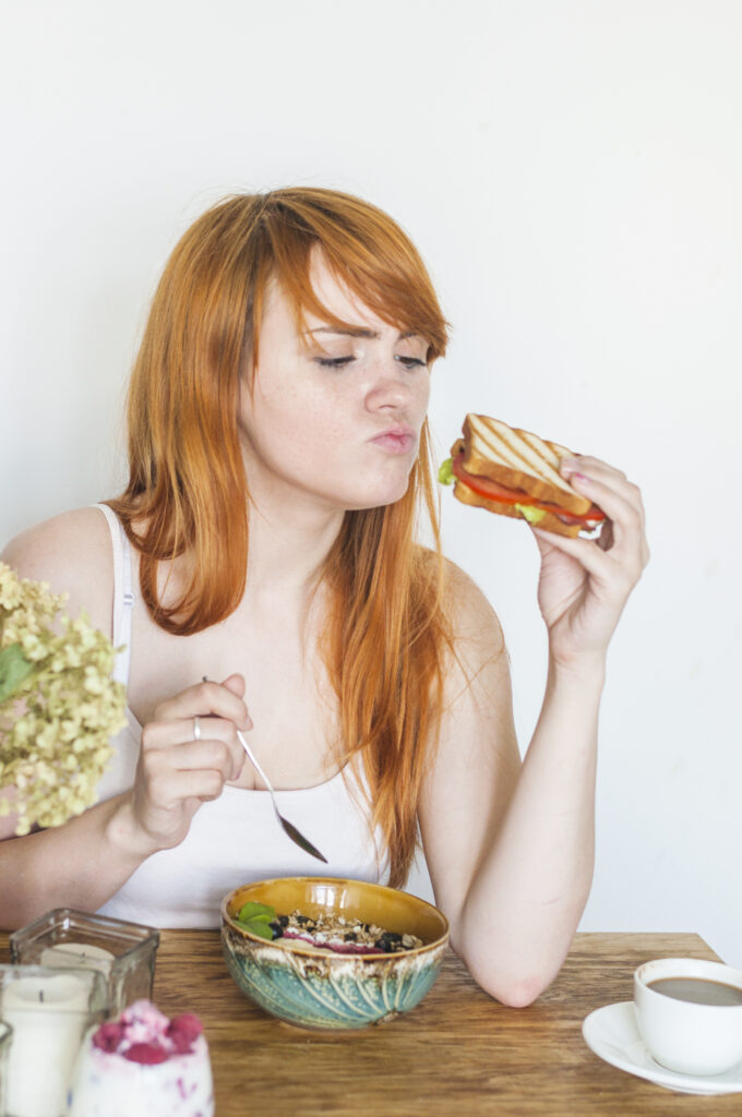 redhead-young-woman-looking-sandwich-with-bowl-oatmeals